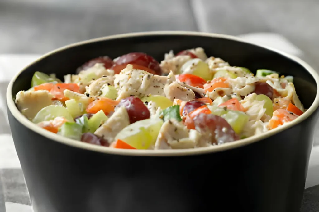 Bowl of creamy chicken salad with halved red grapes, diced celery, and chopped almonds on a wooden table